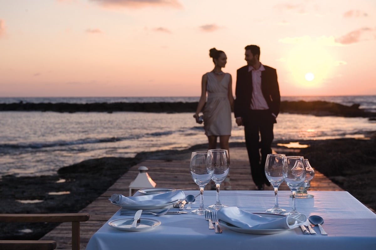 Couples walking along the beach promenade to their dinner table on their Cyprus honeymoon in Paphos with Constantinou Bros Hotels. 